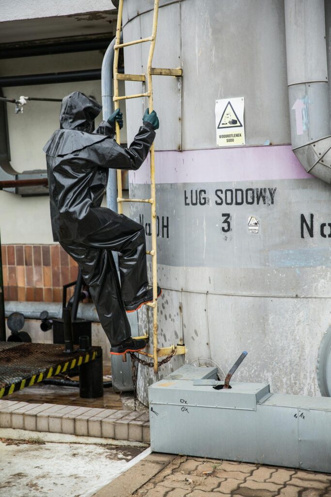 Worker in safety suit climbs industrial tank ladder for maintenance.